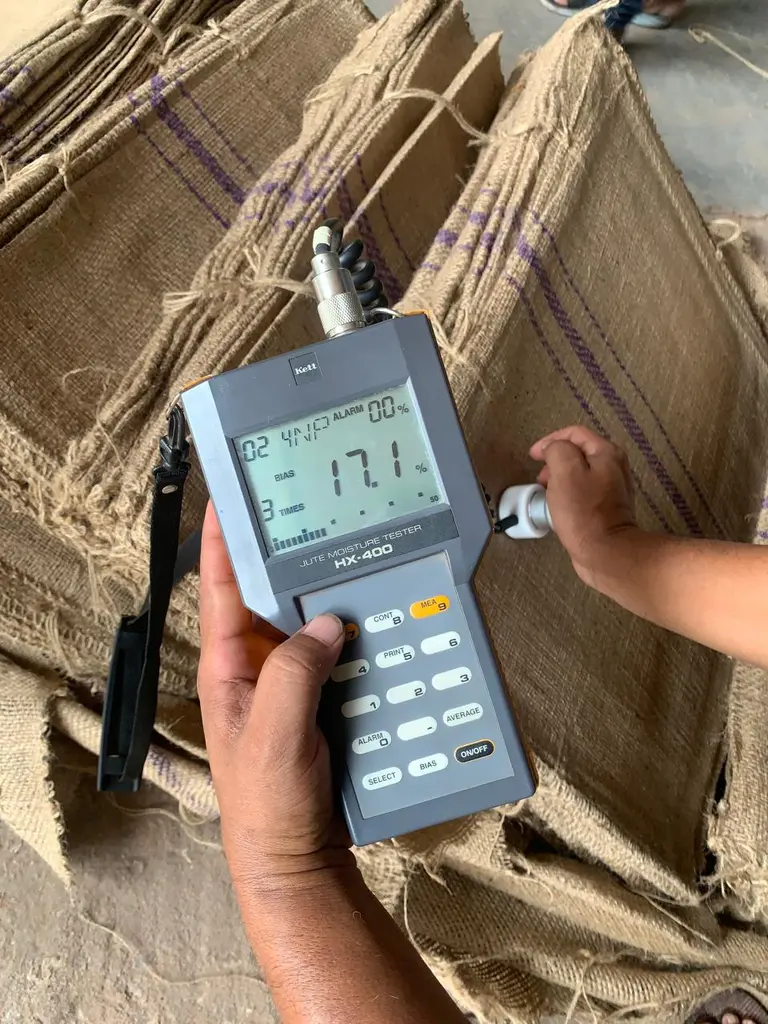 Handheld jute moisture tester showing 17.1 percent reading against pressed bales